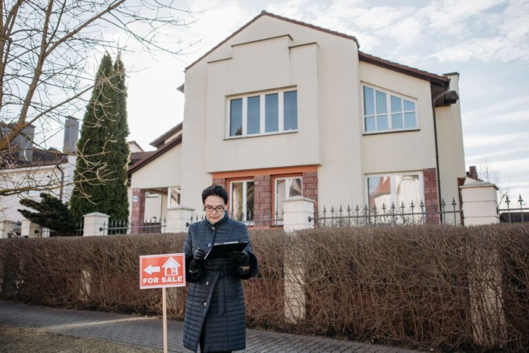Agent nieruchomości przed domem z tablicą na sprzedaż